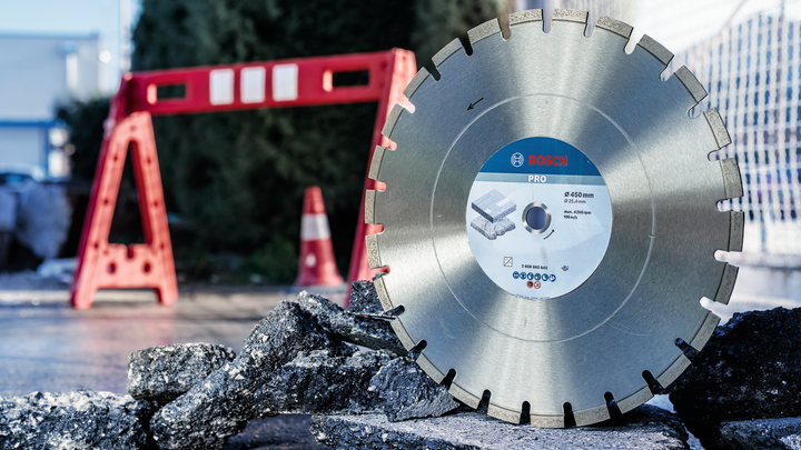 Large diamond saw blade displayed upright on asphalt with broken pavement in front.