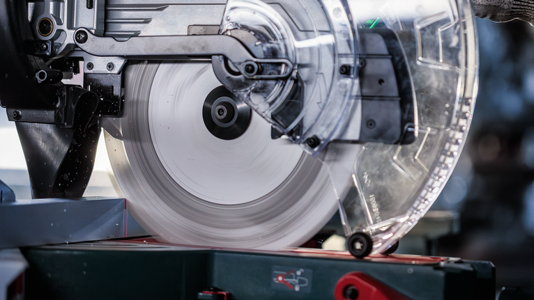 Circular saw blade spinning to cut metal, with protective guard in use.