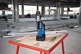 Cordless press tool standing on a worktable in a construction site with metal pipes.