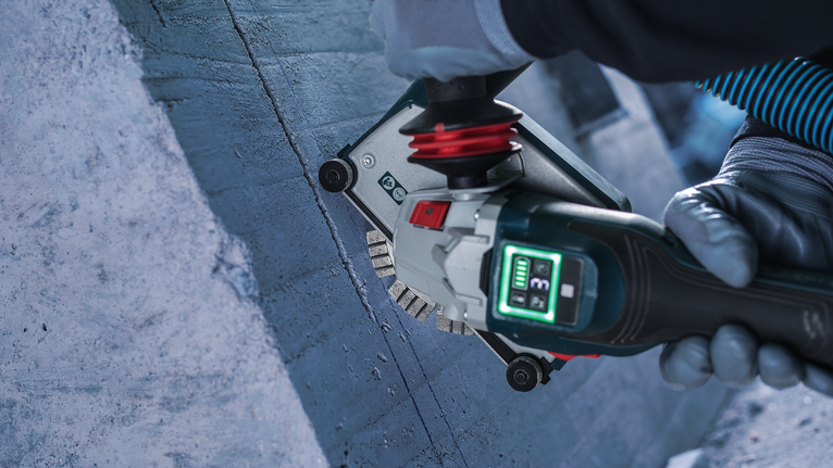 Person wearing safety equipment grinds concrete with a power tool.