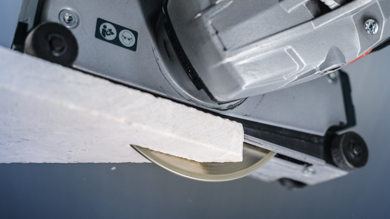 Circular saw blade cutting through a piece of white construction material.