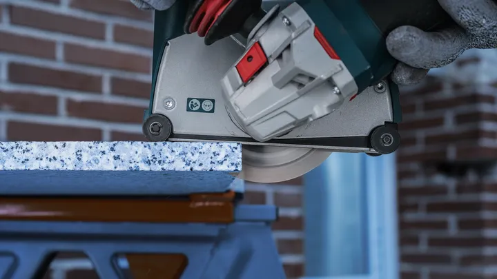 Person wearing safety equipment cuts a stone slab with a circular saw.