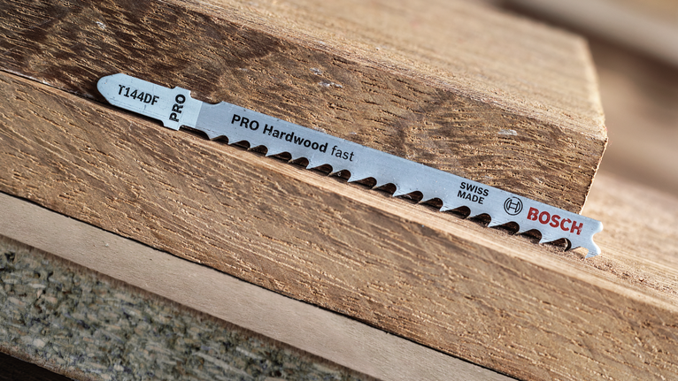 Jigsaw blade lying on stacked pieces of hardwood.