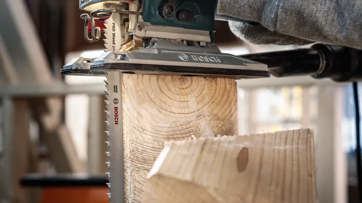 Person wearing safety equipment uses a jigsaw to cut through a wooden beam.