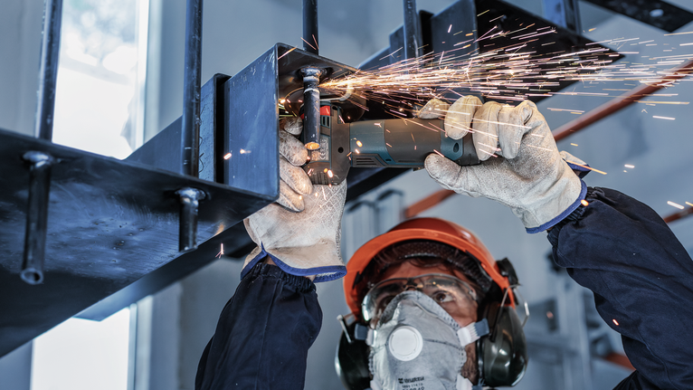 A person wearing safety equipment grinds metal, creating bright sparks.