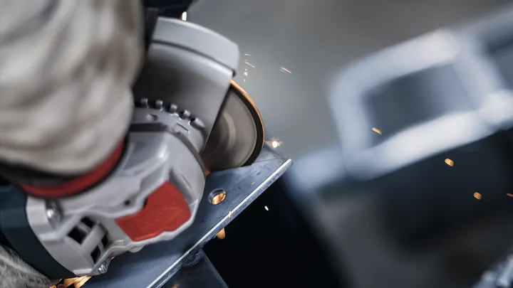 Person wearing safety equipment uses an angle grinder to cut a metal piece.
