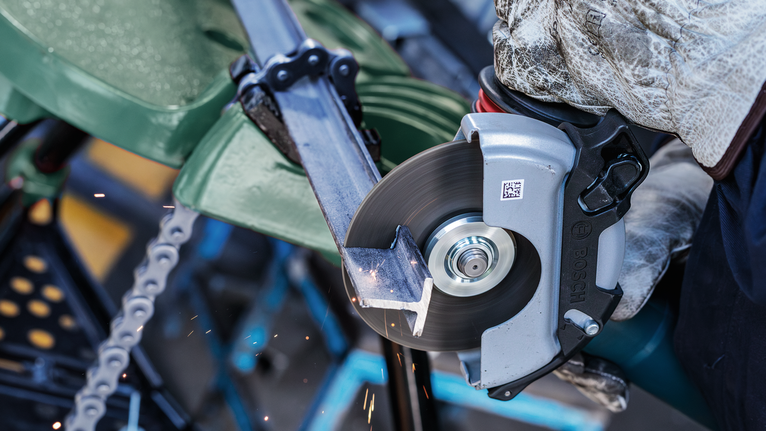Person wearing safety equipment cuts a metal bar with an electric saw.