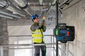 A person wearing safety equipment aligns pipes using a laser leveling tool.
