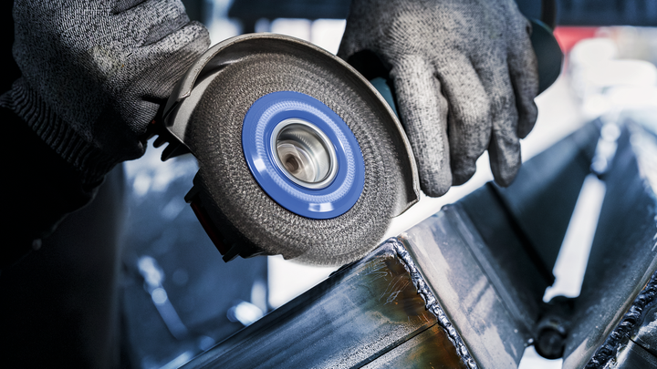 Person wearing safety equipment grinds welded metal beams with an angle grinder.