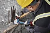 A person wearing safety equipment uses an angle grinder to cut protruding rebar.