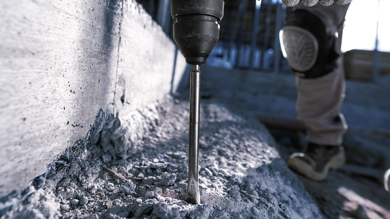 A person wearing safety equipment drills into concrete with a rotary hammer.