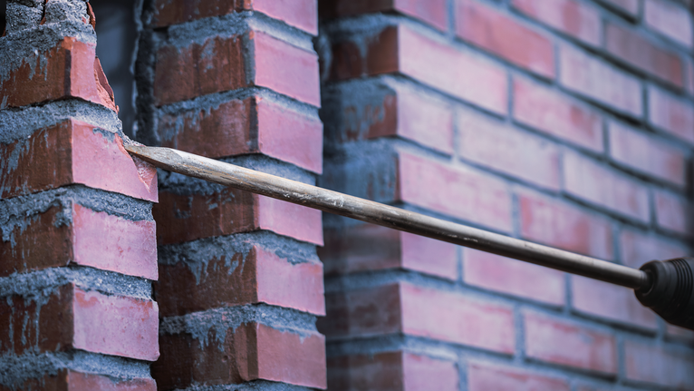 Drill bit making a hole through a brick wall.