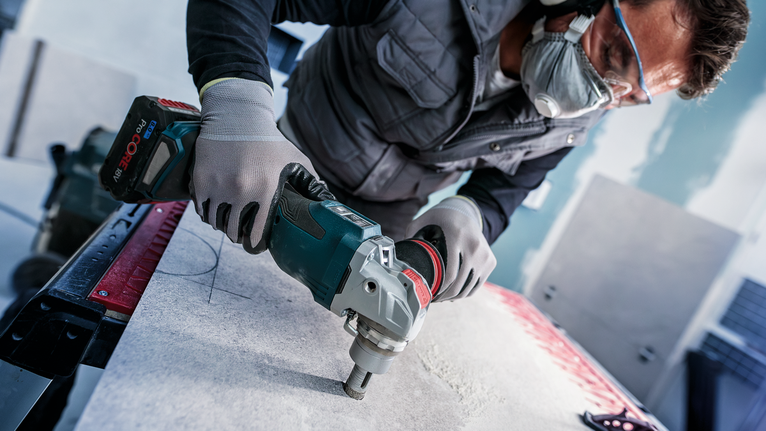 Person wearing safety equipment drills into a stone slab.