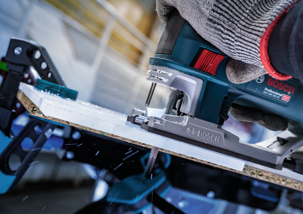 A person wearing safety equipment uses a jigsaw to cut a sheet of wood.