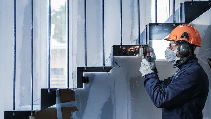 A person wearing safety equipment grinds metal stairs, producing sparks.