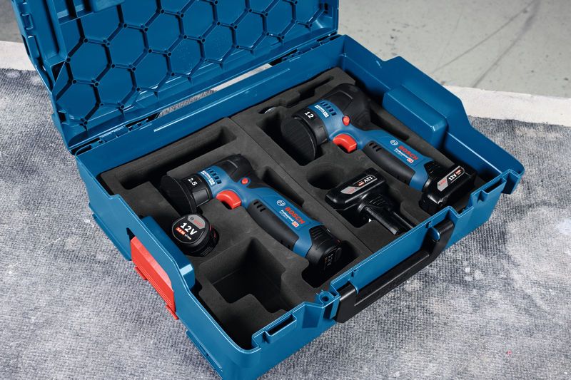 Cordless power tools and batteries organized in a blue carrying case on a work surface.