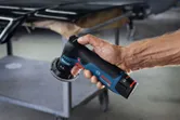 A person holds a random orbit sander near a metal cart in a workshop.