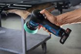 A person uses a cordless polisher with a green foam pad near a workbench.