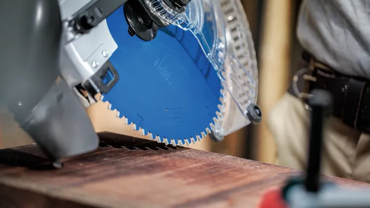 Person wearing safety equipment operates a circular saw on a wooden plank.