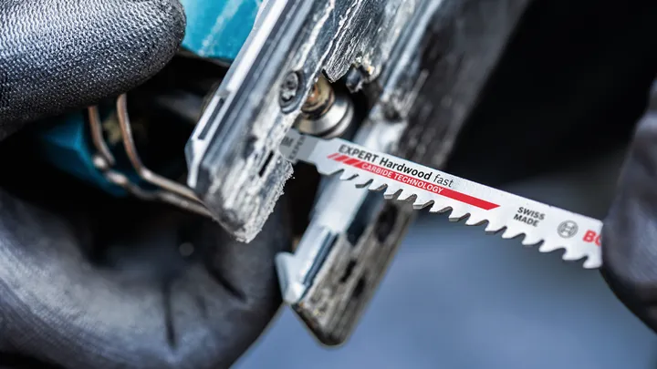 Person wearing safety equipment inserts a jigsaw blade into a power tool.