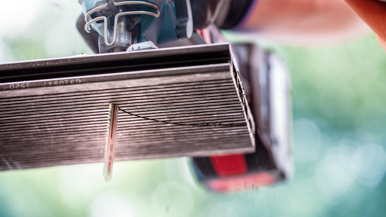 A person wearing safety equipment uses a power saw to cut a ceramic tile.