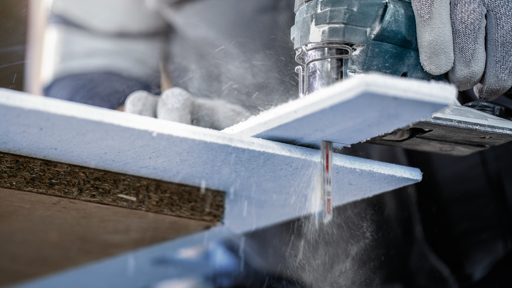 Person wearing safety equipment cuts a foam insulation board using a power jigsaw.