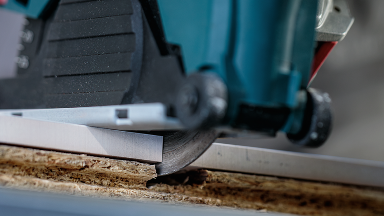 Circular saw cutting through a wooden board along a metal guide.