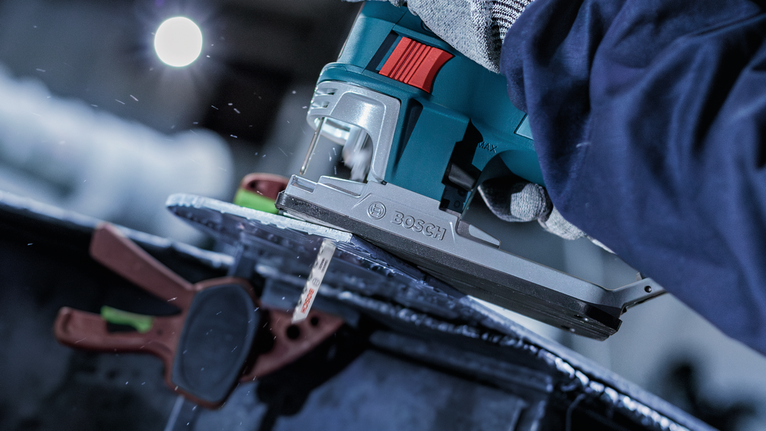 Person wearing safety equipment uses a jigsaw to cut through metal.
