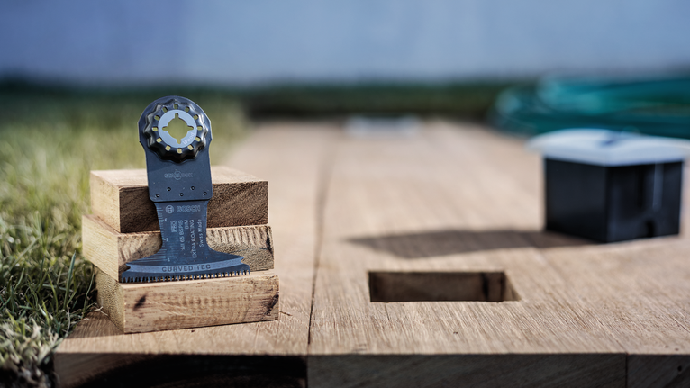 Saw blade attachment resting on stacked wooden blocks beside a cutout in a wooden board.