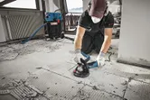 Asmuo, dėvintis apsaugos priemones, šlifuoja betonines grindis betono šlifuokliu.