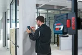 Žmogus žymi betoninį stulpą lazeriniu imtuvu moderniame biuro interjere.