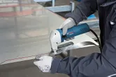 Asmuo, dėvintis apsaugos įrangą, elektrinėmis žirklėmis perpjauna pažymėtą metalinį lakštą.