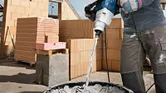 Darbininkas, dėvintis saugos priemones, statybvietėje maišo cementą maišymo mechanizmu.
