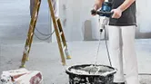 Asmuo, dėvintis apsaugos priemones, maišo medžiagą kibire, naudodamas maišymo mechanizmą.