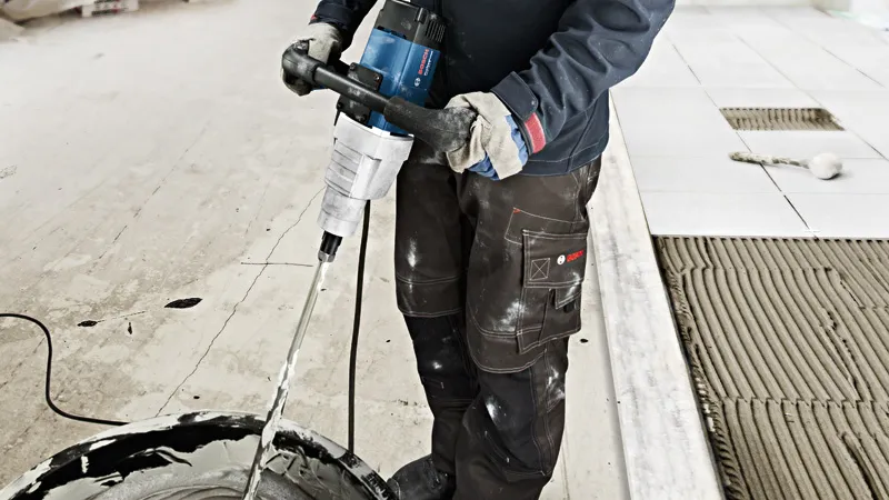 Asmuo, dėvintis apsauginę įrangą, naudoja maišymo mechanizmą statybinėms medžiagoms maišyti.