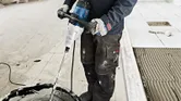 Asmuo, dėvintis apsauginę įrangą, naudoja maišymo mechanizmą statybinėms medžiagoms maišyti.