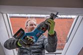 Asmuo, dėvintis apsaugos įrangą, slankiojančiu pjūklu pjauna lango rėmą.