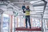 Asmuo, dėvintis saugos įrangą, gręžia betonines lubas statybvietėje.