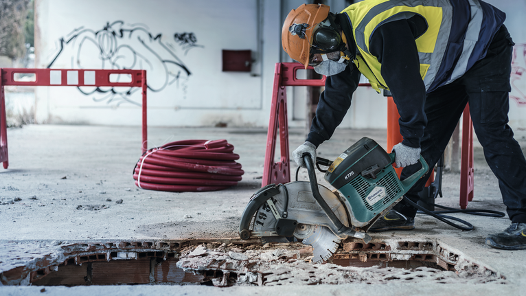 Asmuo, dėvintis apsaugos priemones, diskiniu pjūklu pjauna betonines grindis.