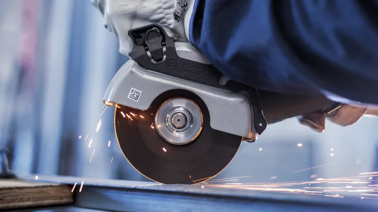 Asmuo, dėvintis apsaugos priemones, pjauna metalą diskiniu pjūklu, sukeldamas kibirkštis.