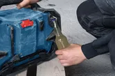 Asmuo statybvietėje naudoja nešiojamąjį radijo stotelę stikliniam buteliui atidaryti.