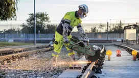Asmuo, dėvintis saugos įrangą, pjauna geležinkelio bėgius elektriniu pjūklu, sukeldamas kibirkštis.