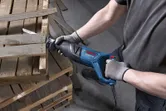 Asmuo, dėvintis apsaugos įrangą, slankiojančiu pjūklu pjausto medinius padėklus.