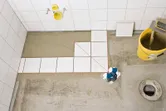 Lazerinis niveliavimo įrankis, projektuojantis raudonas linijas ant grindų plytelių.