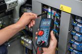 Asmuo matuoja įtampą elektros skydinėje, naudodamas skaitmeninį multimetrą.