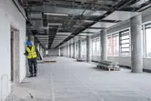 Asmuo, dėvintis apsaugos įrangą, lazeriniu matuokliu patikrina atstumą iki sienos dideliame pastate.