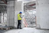 Asmuo, dėvintis apsaugos įrangą, statybvietėje naudoja lazerinį matavimo prietaisą.