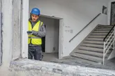 Asmuo, dėvintis apsaugos įrangą, lazeriniu matuokliu matuoja pastato angą.