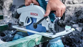 Asmuo, dėvintis apsaugos priemones, pjauna medieną diskiniu pjūklu.