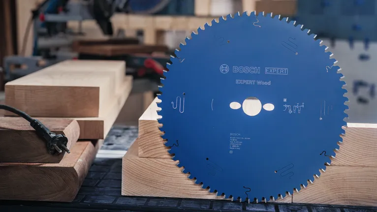 Didelis diskinis pjūklo diskas, stovintis vertikaliai ant medinio darbastalio dailidės dirbtuvėse.